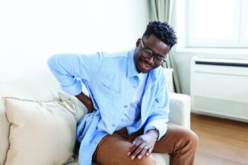 unhappy Man suffering from backache at home. Lower Back Pain . Man feels back pain massaging aching muscles